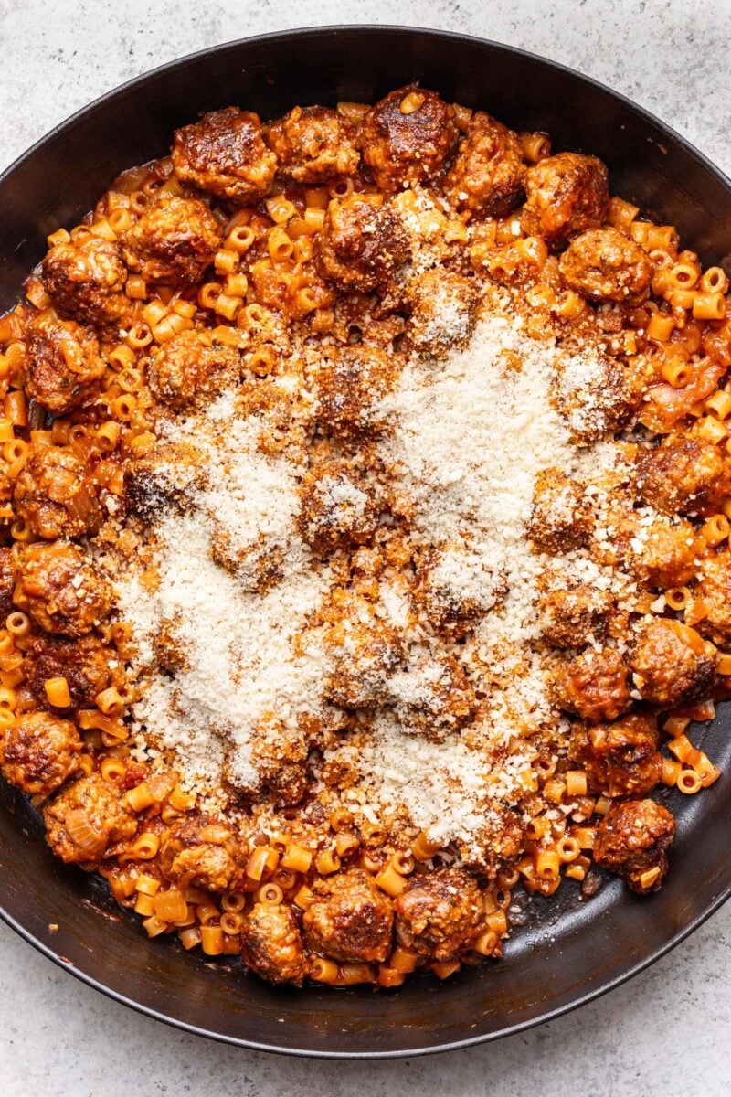 Parmesan cheese sprinkled on top of one pot meatball pasta in a cast iron skillet. 