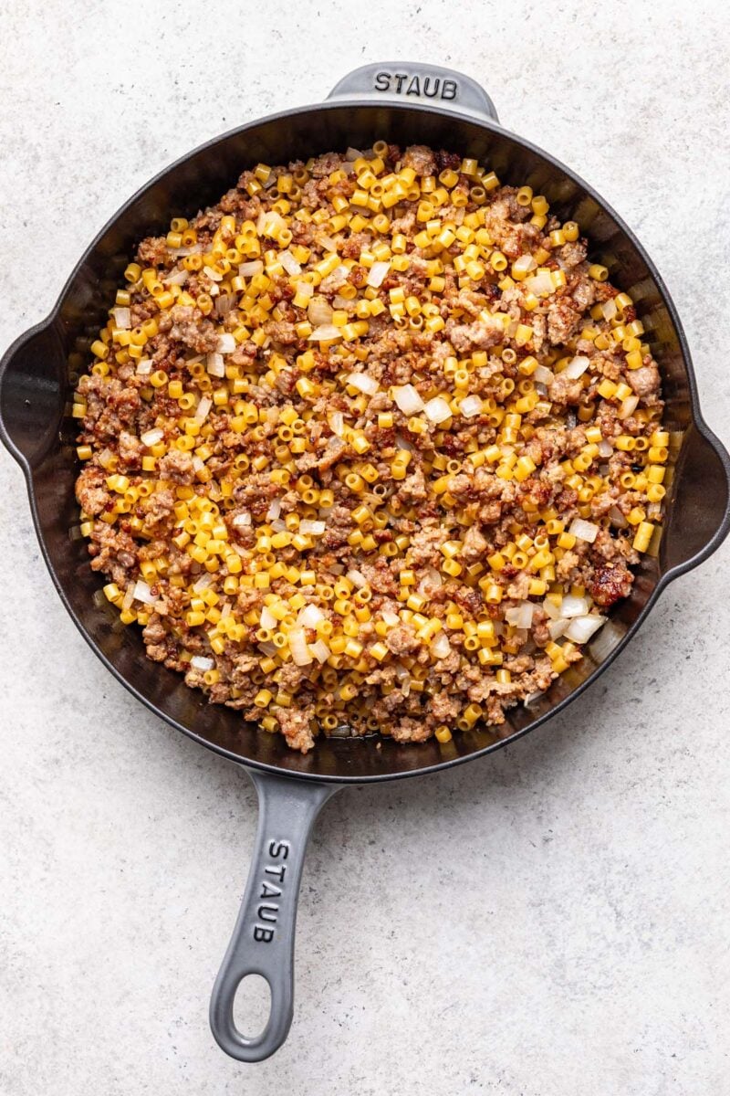 Sausage, wine, onion, garlic, and pasta mixed together in a pan. 