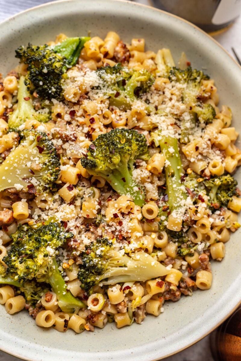 A close up of sausage broccoli pasta in a bowl on a table.