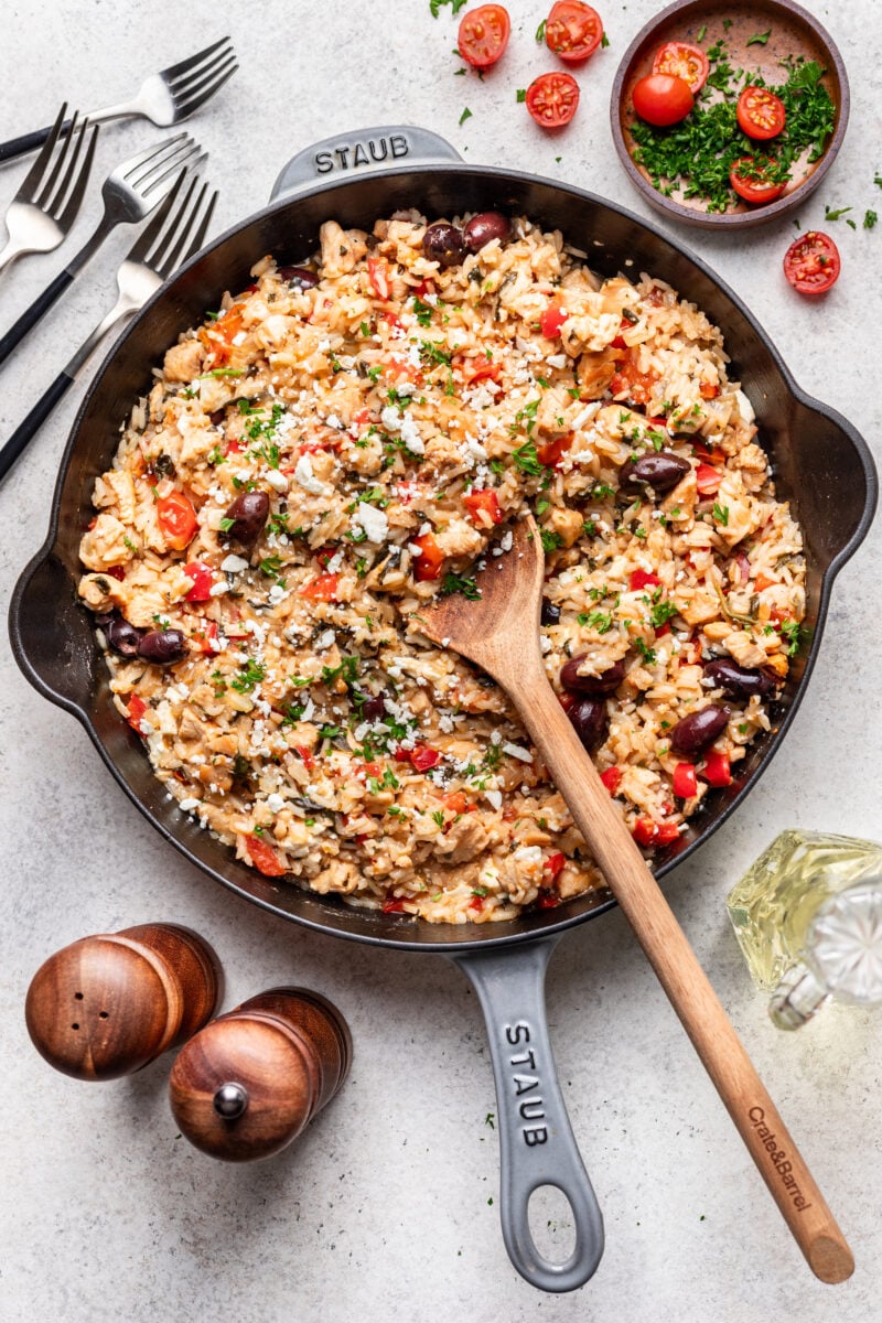 Greek chicken and rice in a cast iron pan with a wooden spoon in it. 