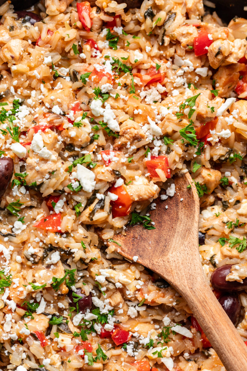A close up of greek chicken and rice with a wooden spoon in it. 