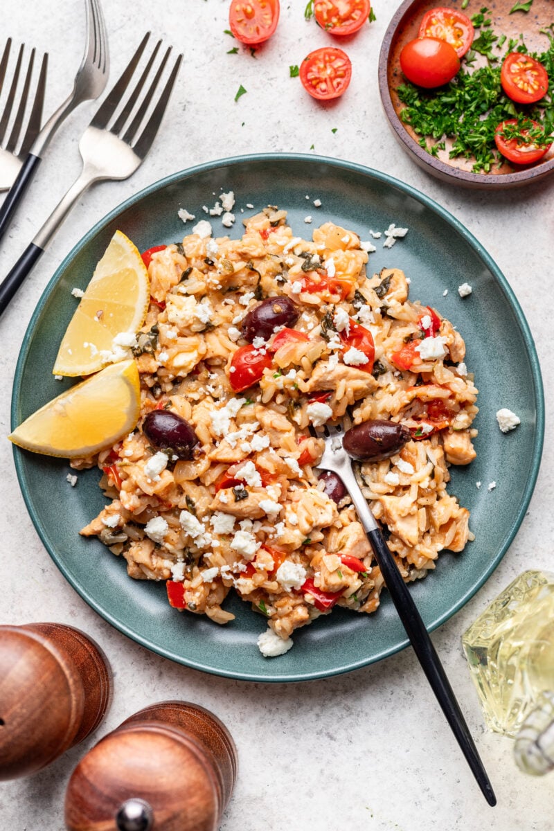 A photo of greek chicken and rice on a plate with lemons on the side and forks in it.
