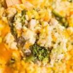 A wooden spoon scooping broccoli cheddar chicken and rice.