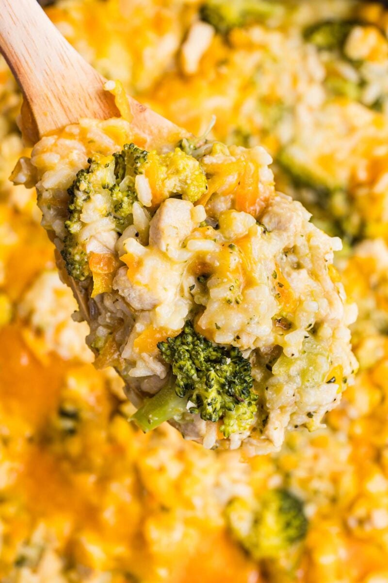 A wooden spoon scooping broccoli cheddar chicken and rice.