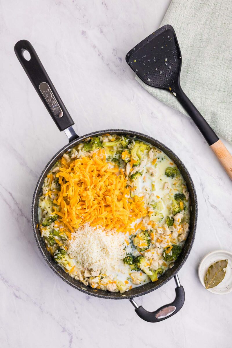 Cheeses on top of broccoli chicken and rice in a saute pan before being mixed in. 