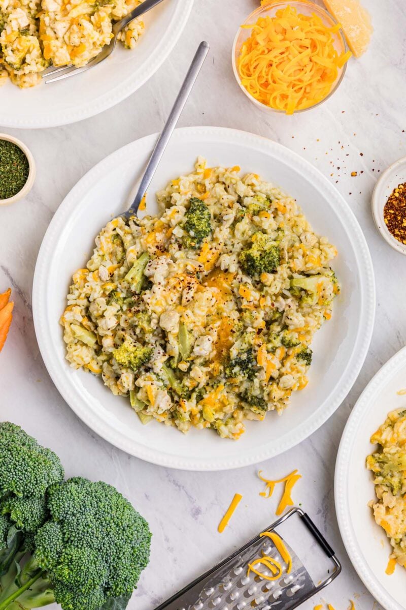 Broccoli Cheddar Chicken and Rice on a white plate with a fork in it and fresh broccoli on the side. 