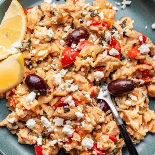 A photo of greek chicken and rice on a plate with lemons on the side and forks in it.