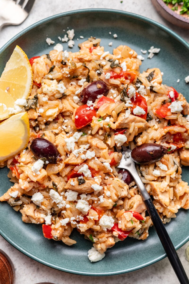A photo of greek chicken and rice on a plate with lemons on the side and forks in it.