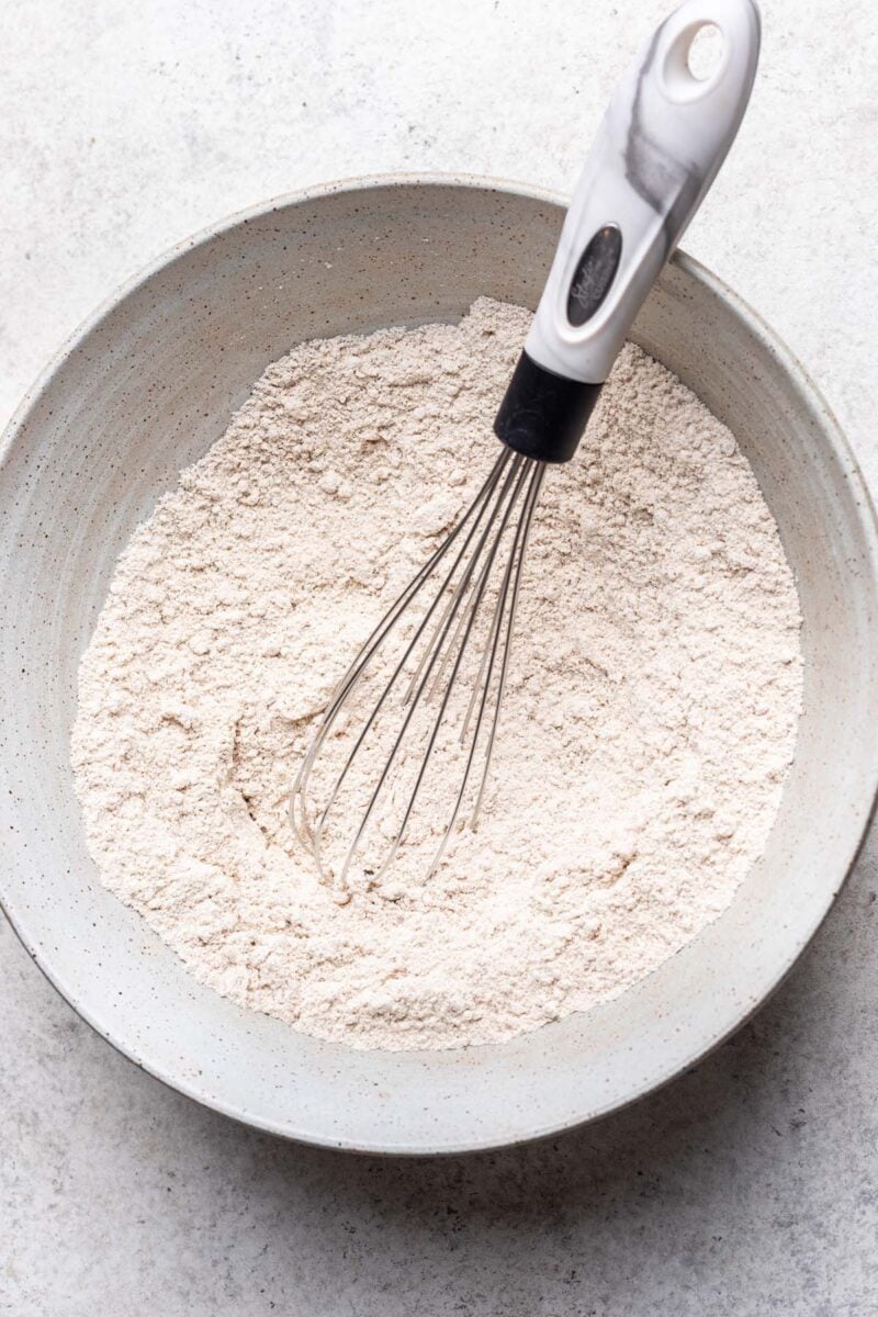 A whisk mixing together dry ingredients for oat flour pancakes in a bowl. 