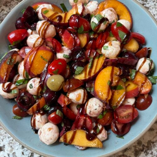 Peach Caprese Salad drizzled with balsamic glaze in a blue bowl