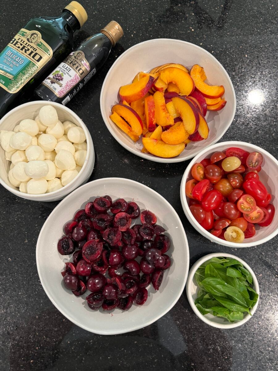Ingredients for a summer stone fruit salad in bowls on a black counter