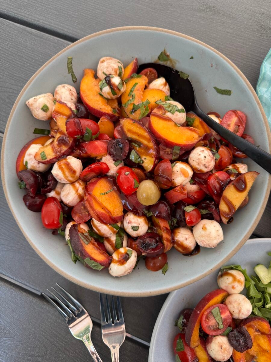 Peach Caprese Salad in a blue bowl with a black spoon