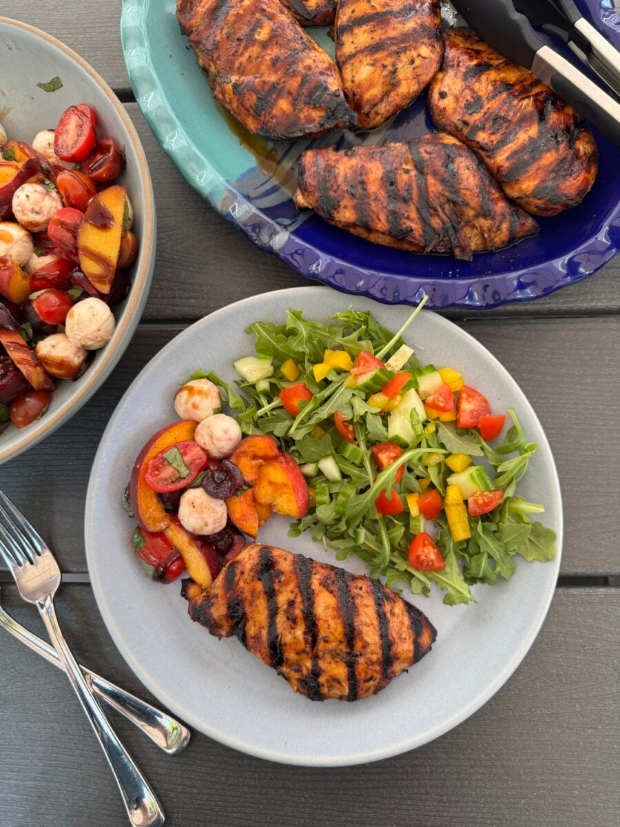 Peach caprese salad on a plate with grilled chicken and an arugula salad.