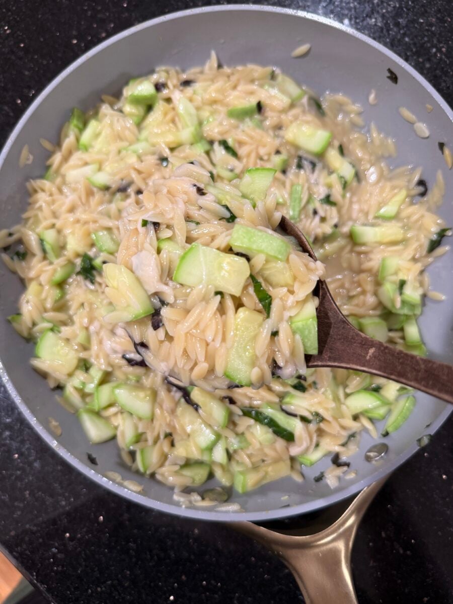 A ladle scooping out a serving of zucchini orzo