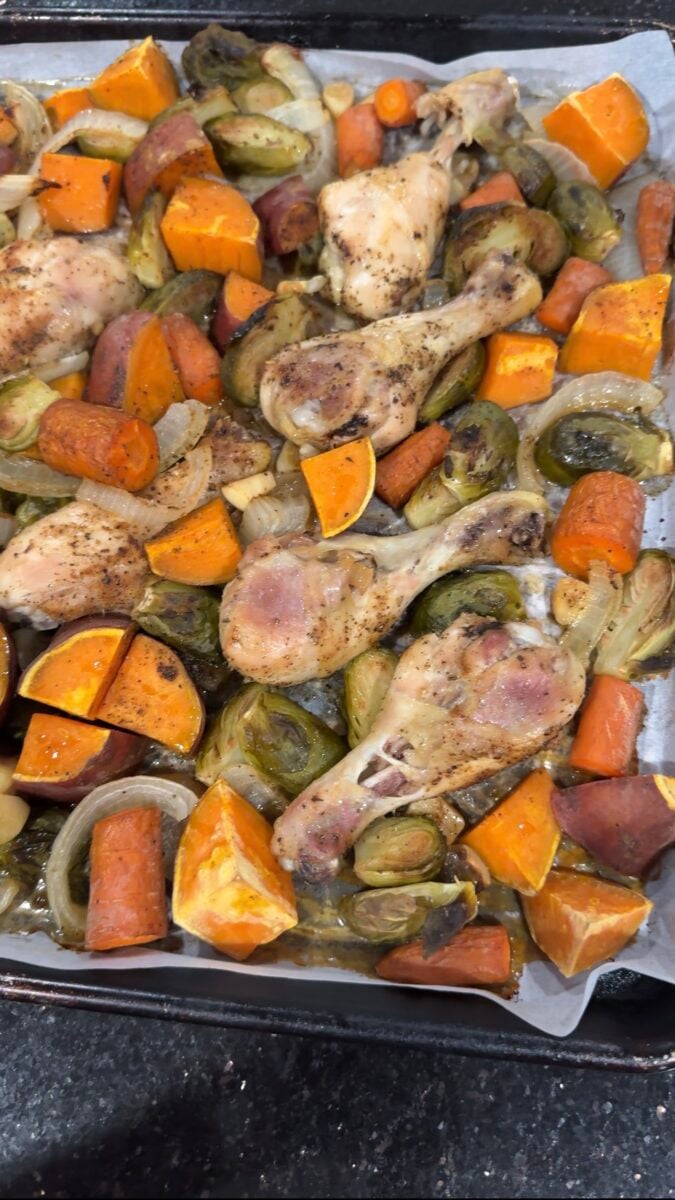 a close up of chicken drumsticks and sweet potatoes on a pan