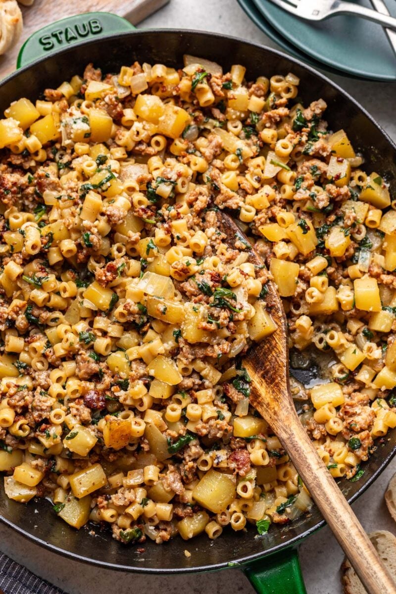 A cast iron skillet filled with zuppa toscana pasta and a wooden spoon in it.